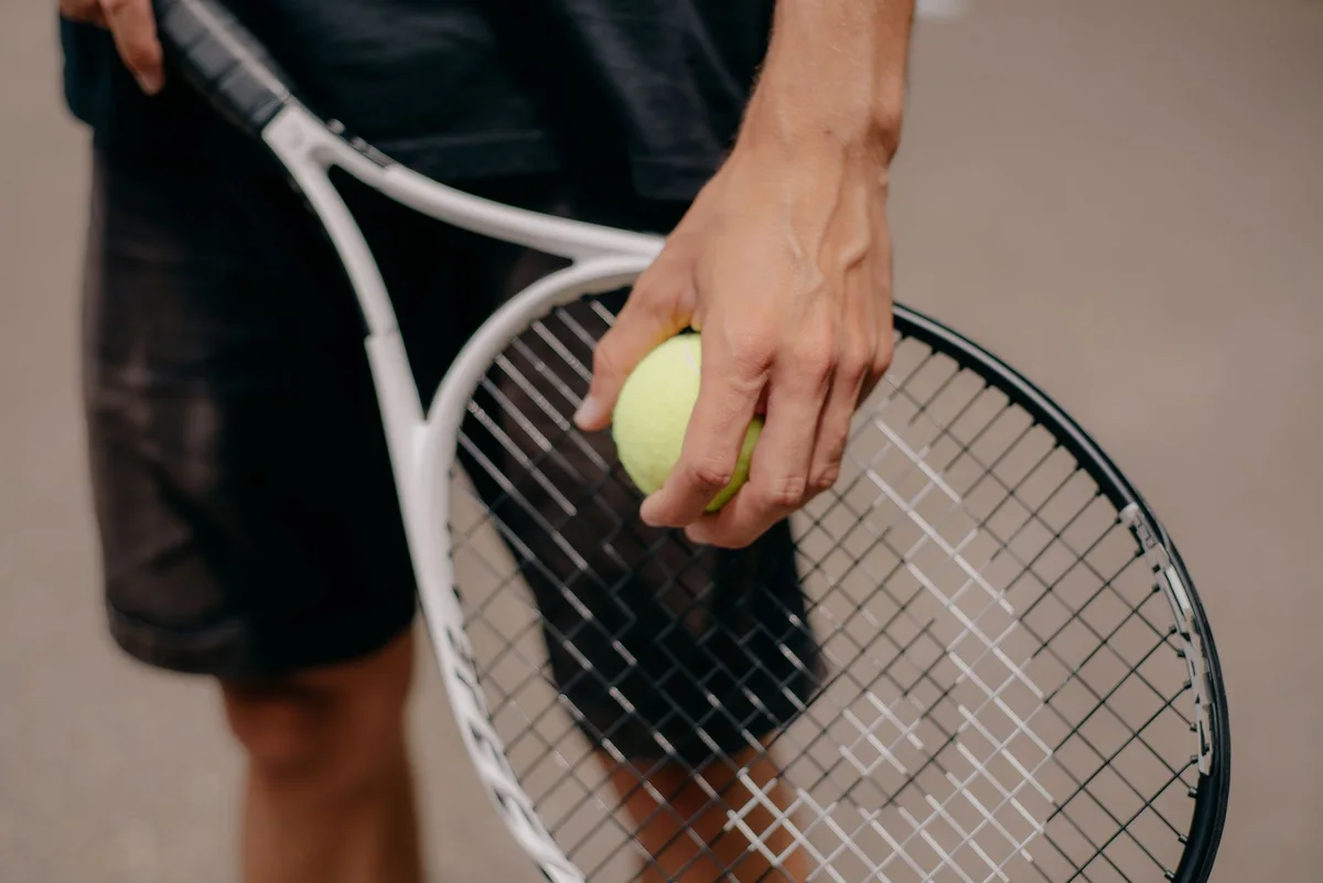 Mãos segurando raquete e bola antes de entrar em quadra